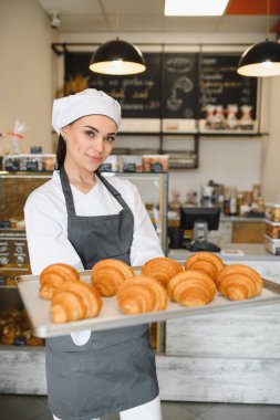 Kadın fırıncı gururla sunar taze pişmiş altın rengi kruvasan tepsisini büyüleyici fırınında, sıcaklık ve yetenek saçan