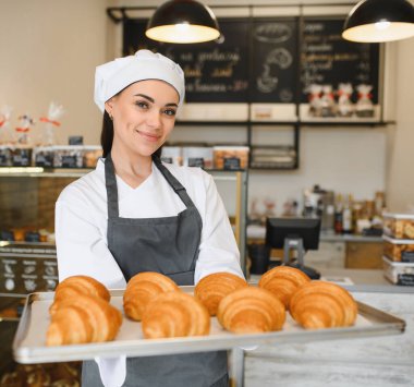 Fırınında bir tepsi altın rengi kruvasan sunan dişi fırıncı, pişirme becerilerinin lezzetli sonuçlarını gözler önüne seriyor.