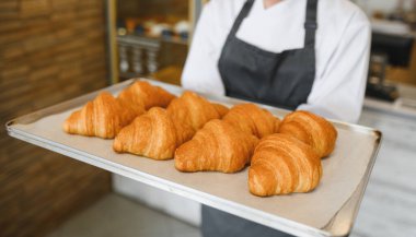 Baker bir tepsi altın sarısı kruvasan sunuyor. Pastanenin hamur işlerindeki uzmanlığını gösteriyor.