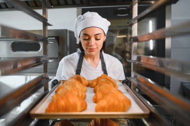 Profesyonel fırıncı, endüstriyel fırına altın kahverengi kruvasan koyar. Ticari mutfakta mükemmel pişirme garantisi verir.