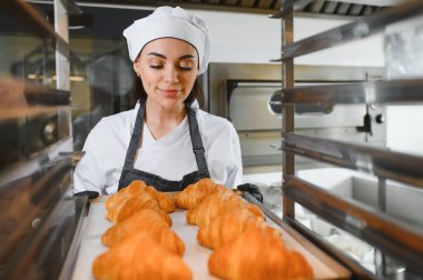 Profesyonel fırıncı gururla sunar bir tepsi mükemmel altın kruvasan, ticari bir mutfakta pişirme uzmanlığının sonucunu sergiliyor