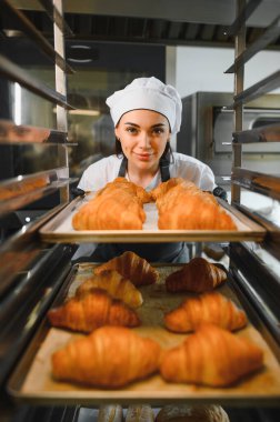 Profesyonel fırıncı bir fırın mutfağındaki rafa altın rengi kruvasan koyuyor.