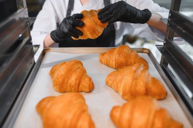 Fırında pişmiş altın kruvasanları düzenleyen siyah eldivenli fırıncı.