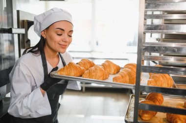 Baker, sıcak bir fırının sıcak atmosferiyle çevrili tepside yeni pişmiş kruvasanların enfes aromasının tadını çıkarıyor.