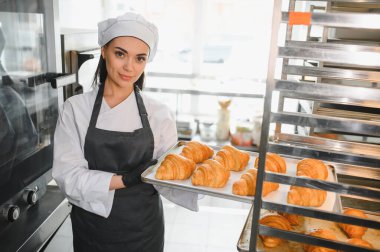 Profesyonel fırıncı bir tepsi altın kruvasan sunuyor. Ticari bir mutfakta pişirme uzmanlığının sonucunu sergiliyor.