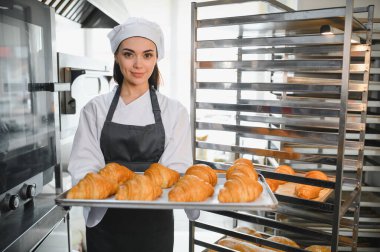 Profesyonel fırıncı bir tepsi altın kruvasan sunuyor. Ticari bir mutfakta pişirme uzmanlığının sonucunu sergiliyor.