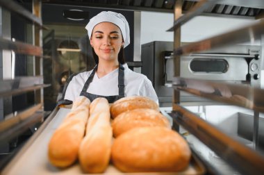 Profesyonel fırıncı gururla bir tepsi taze ekmek ve ekmeği ticari bir mutfakta sunar.