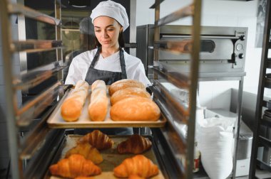 Profesyonel bir fırında ekmek tepsileri, somunlar ve kruvasanlar düzenleyen fırıncı, fırında pişirme sanatını sergiliyor.