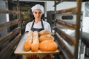 Fırıncı bir tepsi sunar. Taze fırında baget ve yuvarlak ekmeklerle dolu. Ticari mutfak ortamında.