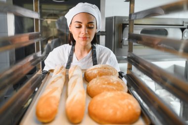 Profesyonel fırıncı, taze pişmiş baget ve mutfaktaki fırın tepsisinde soğuyan yuvarlak somunların enfes aromasının tadını çıkarıyor.