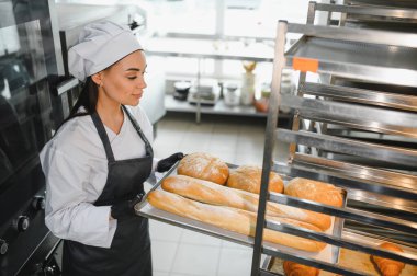 Profesyonel fırıncı ekmek tepsisi ve yuvarlak somunları ticari bir fırın mutfağındaki metal soğutma rafına yerleştiriyor.