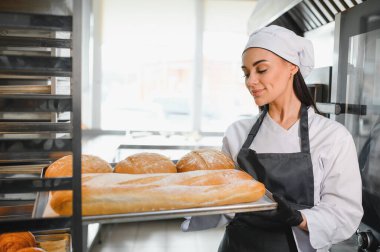 Fırıncı kadın fırında ya da ticari mutfakta çeşitli taze fırınlanmış somun ekmekleri gururla sunar.