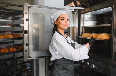 Profesyonel fırıncı fırındaki büyük bir sanayi fırınından taze pişmiş somun ekmeği alıyor.