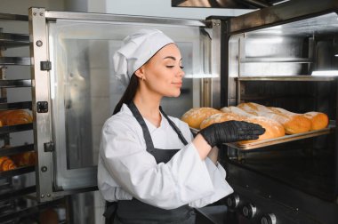 Siyah eldiven giymiş kadın fırıncı fırından taze pişmiş ekmek tepsisini alıyor.
