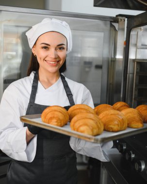 Profesyonel fırıncı gülümseyerek ve elinde bir tepsi altın rengi kruvasan tutarak pişirme uzmanlığının leziz sonuçlarını sergiliyor.