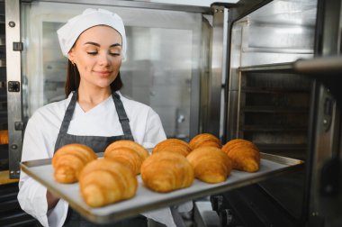 Profesyonel fırıncı taze pişmiş kruvasan kokusu alıyor, ticari mutfakta fırın tepsisi tutuyor.