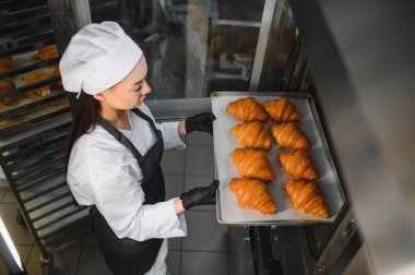 Profesyonel bir fırıncı, büyük bir endüstriyel fırına bir tepsi altın rengi kruvasan koyar.