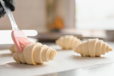 Silikon fırça kullanarak kruvasanları yumurta fırçasıyla kaplamak, profesyonel mutfakta pişirmek için hamur işleri hazırlamak.