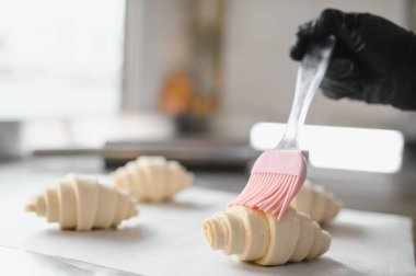 Profesyonel bir mutfakta yeni yapılmış kruvasanları parlatarak lezzetli hamur işleri yapmak için özenle ve ustalıkla pişirmeye hazırlanıyorlar.