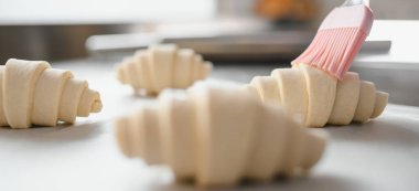 Pişirmeden önce yumurta yıkama ile ovalanan çiğ kruvasanların yakın çekimi, bir fırında hazırlık sürecini gösteriyor