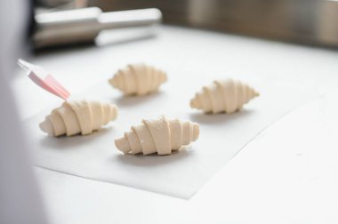 Profesyonel bir fırın mutfağında fırçayla yeni yapılmış kruvasanları parlatarak lezzetli hamur işleri yaratıyorlar.