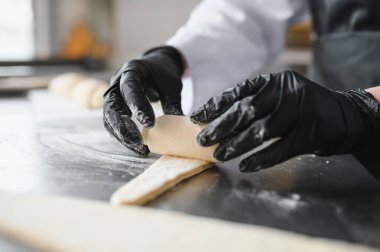 Siyah eldiven giyen fırıncı un kaplı metal masaya hamur rulo, lezzetli kruvasanlar yapmaya hazırlanıyor