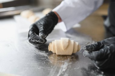 Fırında kruvasan hamurunu ustalıkla hazırlayan siyah eldivenli fırıncı hamur işi yapma sanatını sergiliyor.