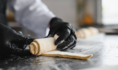 Siyah eldiven giyen fırıncı profesyonel bir mutfakta lezzetli kruvasanlar hazırlamak için bir parça hamur topluyor.