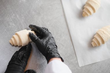 Siyah eldiven giyen fırıncı lezzetli aromalarla dolu fırın mutfağındaki metal bir masada kruvasan hamuru ustalıkla hazırlıyor.