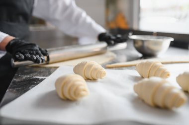 Profesyonel bir mutfakta hamuru yuvarlıyor ve kruvasan şekillendiriyor. Lezzetli hamur işlerinin hazırlanmasına odaklanıyor.