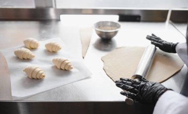 Fırıncı ustalıkla hamuru merdaneyle atıyor, profesyonel fırın mutfağında lezzetli kruvasanlar yapmaya hazırlanıyor.