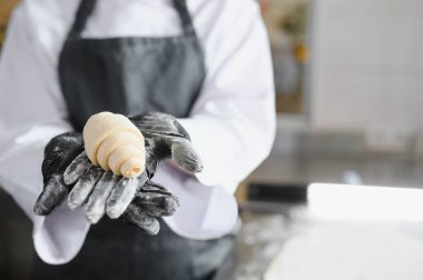 Siyah eldiven giyen fırıncı fırında taze pişmiş kruvasan sunuyor. Pasta hazırlama sanatını ön plana çıkarıyor.
