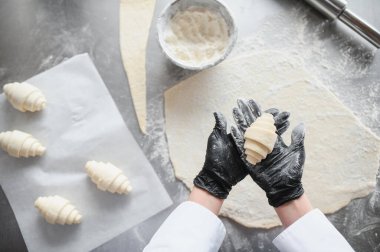 Fırında yeni yapılmış kruvasan ve diğer ayçöreği ve hamuru gösteren siyah eldivenler giyen fırıncı.