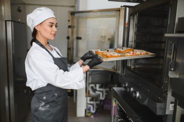 Profesyonel fırıncı siyah eldiven giyip profesyonel bir fırından lezzetli hamur işleri alıyor.