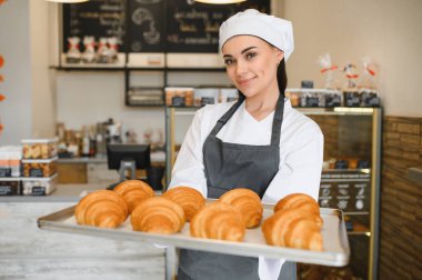 Dişi fırıncı gururla sunar bir tepsi altın kahverengi kruvasan, fırının lezzetli hamur işlerini sunar