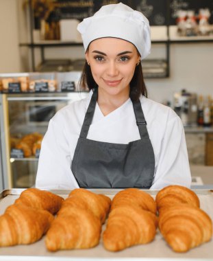 Dişi fırıncı, lezzetli altın kruvasan tepsisini sunuyor, fırın ortamında pişirme becerilerini sergiliyor.