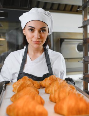 Profesyonel fırıncı bir tepsi altın kruvasan sunuyor. Ticari bir mutfakta pişirme uzmanlığının sonucunu sergiliyor.