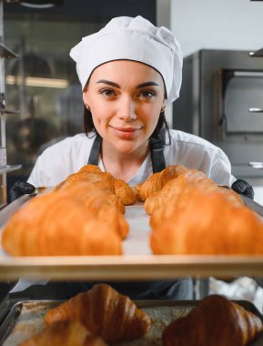 Profesyonel fırıncı gururla sunar bir tepsi altın kahverengi kruvasan, ticari bir mutfakta pişirme uzmanlığının sonucunu sergiliyor