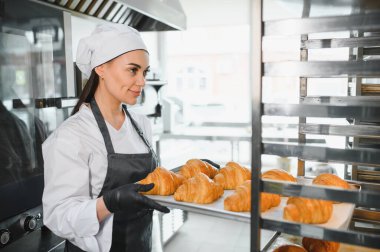 Profesyonel bir fırıncı soğutma rafına bir tepsi altın rengi kruvasan yerleştiriyor, müşteriler tarafından beğenilmeye hazır.