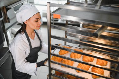 Profesyonel bir fırıncı, ticari bir fırının soğutma rafına dikkatlice bir tepsi altın kahverengi kruvasan koyar. Mükemmel bir doku ve tat sağlar.