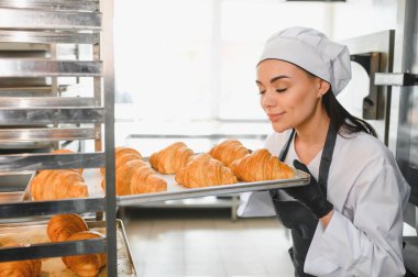 Kadın fırıncı, hareketli bir ticari mutfakta çalışırken taze pişmiş kruvasanın enfes aromasının tadını çıkarıyor.