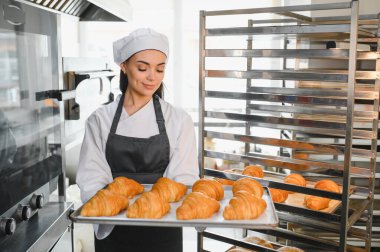 Profesyonel fırıncı gururla altın kahverengi kruvasan tepsisini sergiliyor, ticari mutfağındaki pişirme uzmanlığının sonuçlarını sergiliyor.