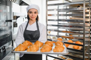Profesyonel fırıncı bir tepsi altın kruvasan sunuyor. Ticari bir mutfakta pişirme uzmanlığının sonucunu sergiliyor.