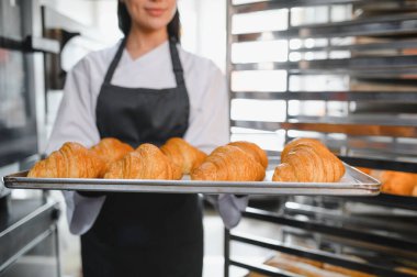 Profesyonel fırıncı, geleneksel bir pastanenin kalitesini ve zanaatkarlığını sergileyen, bir tepsi mükemmel kahverengi kruvasan sunuyor.