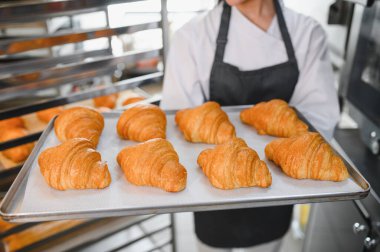 Baker, bir tepsi mükemmel kahverengi kruvasan sunuyor. Sanatçılık ve pişirme azmini gözler önüne seriyor.