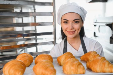 Gülümseyen fırıncı altın rengi kruvasan tepsisini sunar, fırının ürünlerinin kalitesini ve tazeliğini gözler önüne serer.