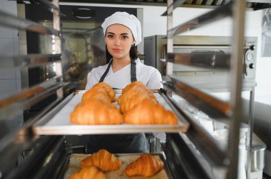 Profesyonel bir fırıncı bir fırında büyük bir endüstriyel fırına bir tepsi altın kahverengi kruvasan koyar.