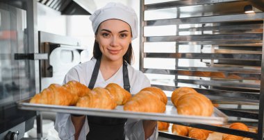 Profesyonel bir fırıncı bir tepsi altın rengi kruvasan sunuyor. Ticari bir mutfakta pişirme uzmanlığının sonucunu sergiliyor.