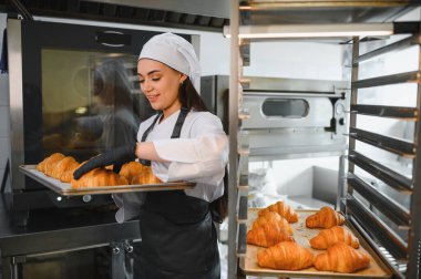 Profesyonel bir fırıncı ticari fırın mutfağında rafa sıcak kruvasan koyar ve fırın sanatını sergiler.