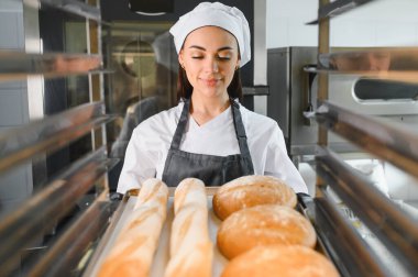 Profesyonel fırıncı gururla bir tepsi taze ekmek ve baget sunar, fırın ortamında sıkı çalışmasının sonucunu sergiler.